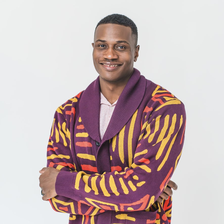 Miles Ukaoma in a studio portrait wearing a patterned jacket, arms crossed